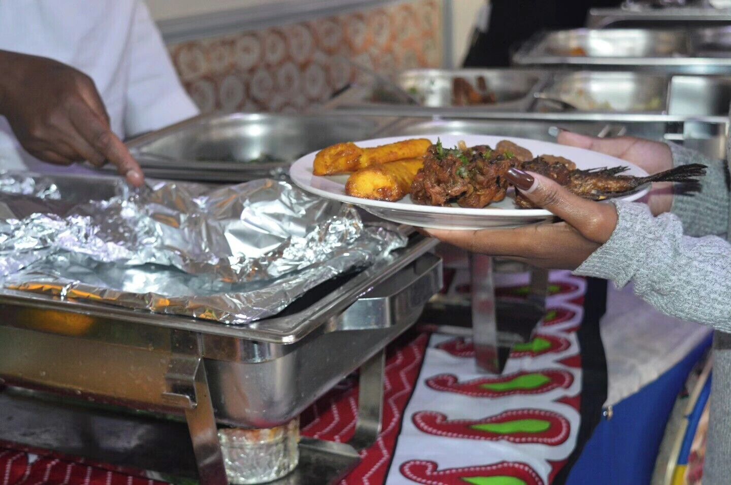 Montaje de bufé con diversos platos y una persona sirviendo comida.