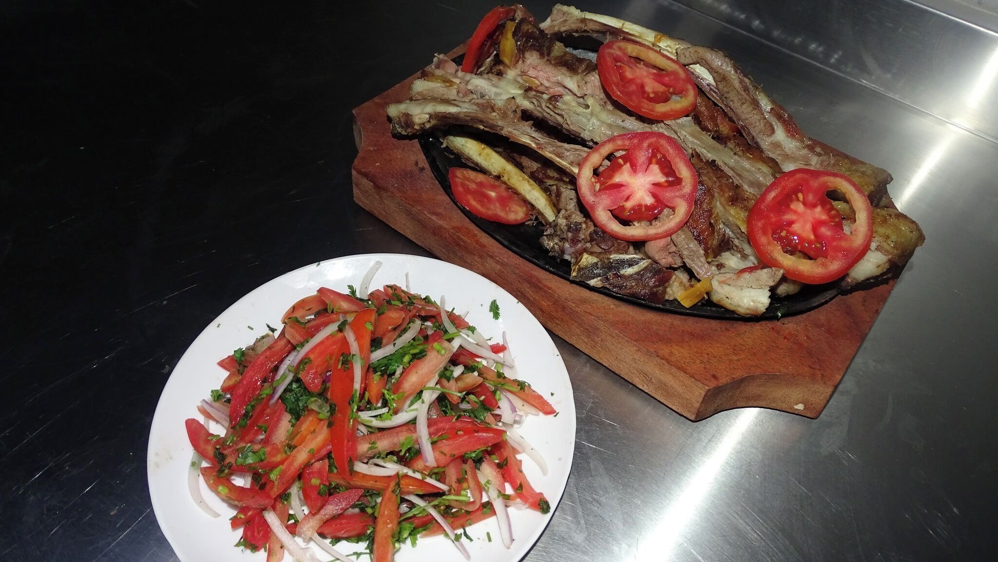 Un plato de chuletas de cordero a la parrilla con tomates y una ensalada.
