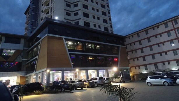Een meerlaags hotel met een modern ontwerp, met een opvallend hoekgebouw met verlichte ramen en een parkeerplaats met meerdere auto's.