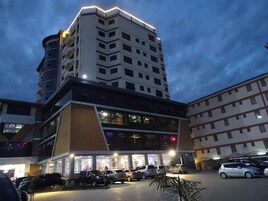 A multi-story hotel with a modern design, featuring a prominent corner building with illuminated windows and a parking area with several cars.