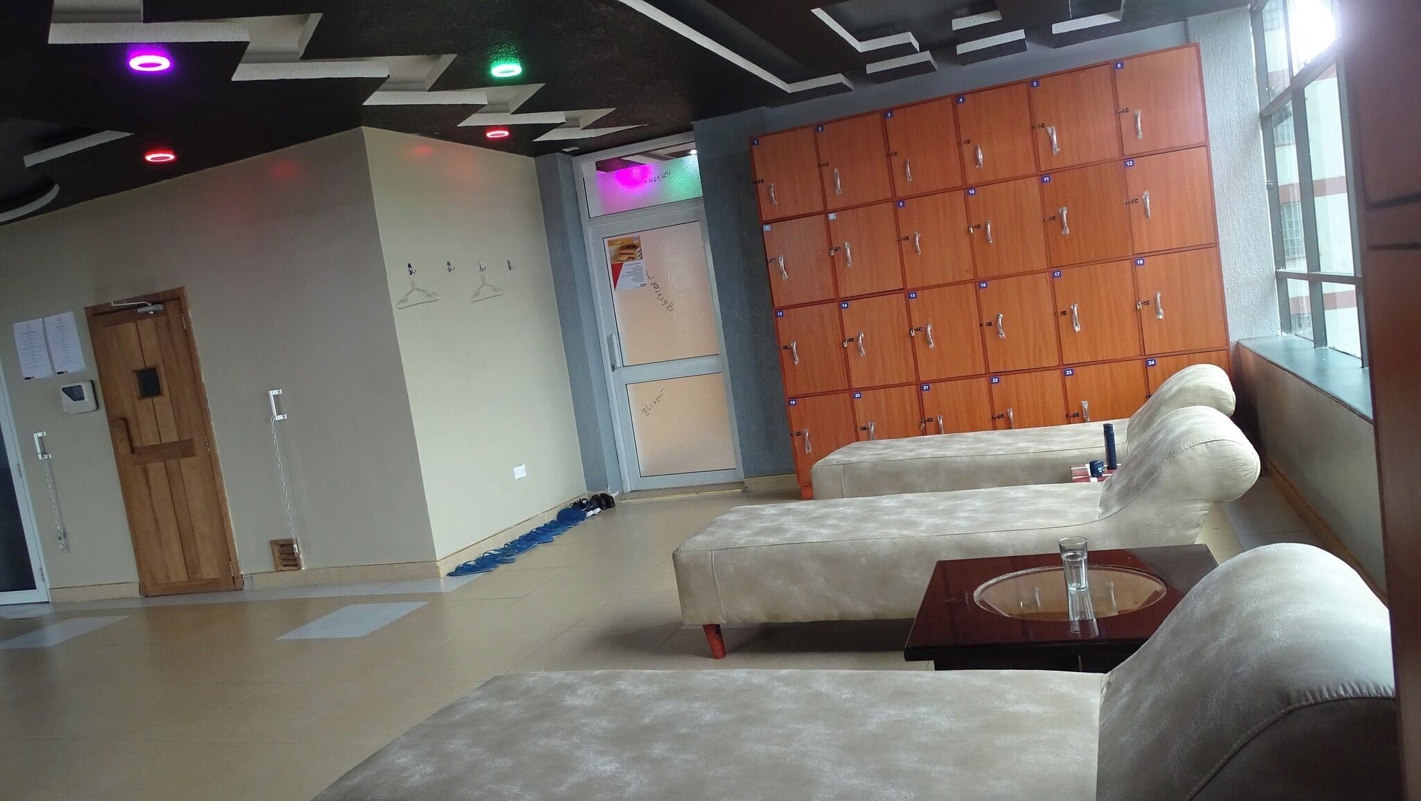 Een hotel lobby met een zithoek, houten kluisjes en een deur met een kettinggrendel.
