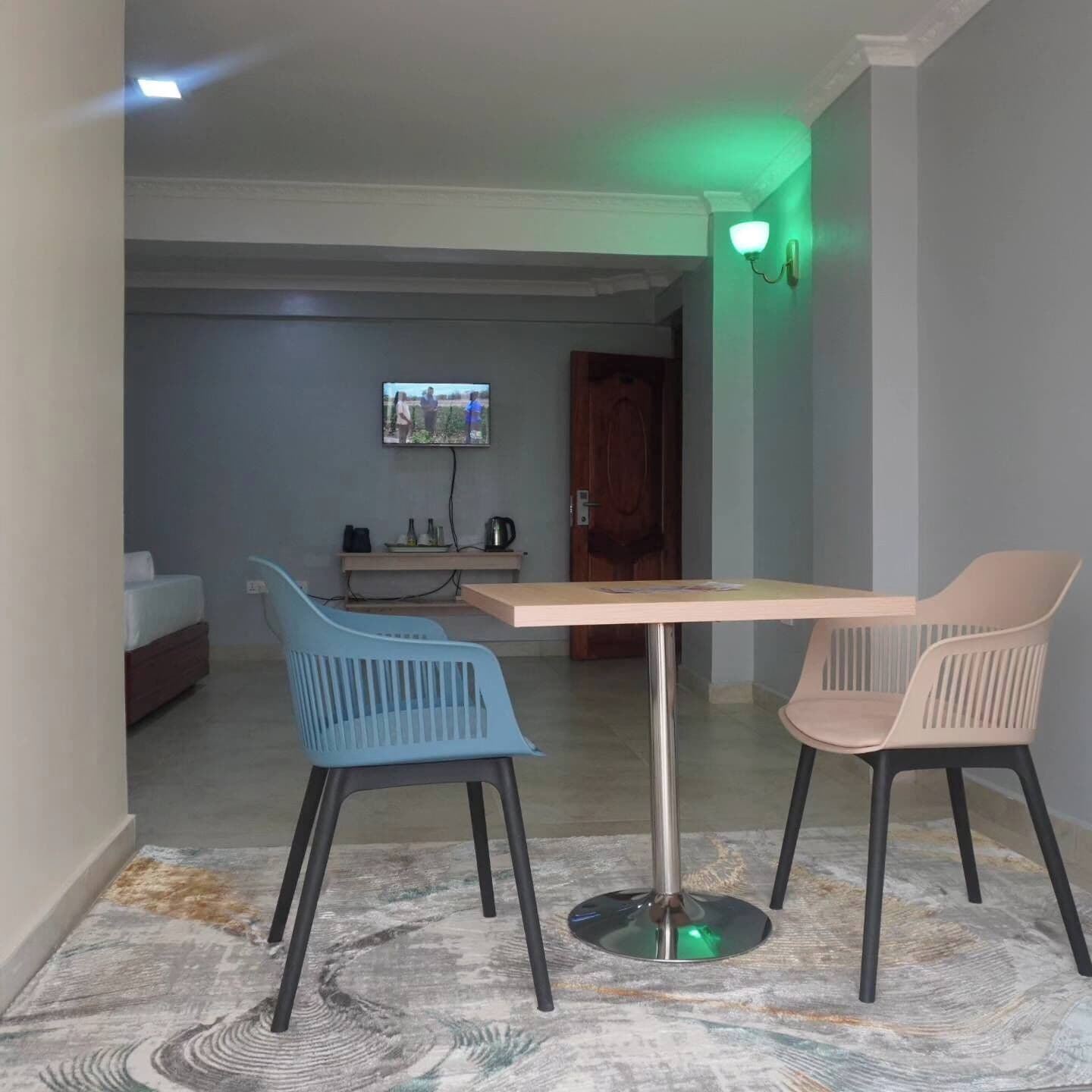 A dining area with a table and two chairs, a television in the background, and a door leading to another room.