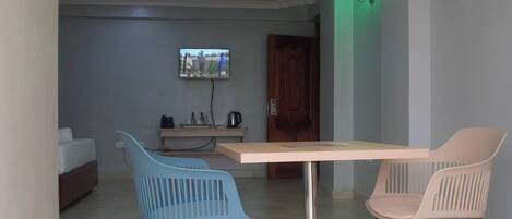 A dining area with a table and two chairs, a television in the background, and a door leading to another room.