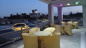Een terras met rieten meubels en uitzicht op een parkeerplaats en gebouwen op de achtergrond.
