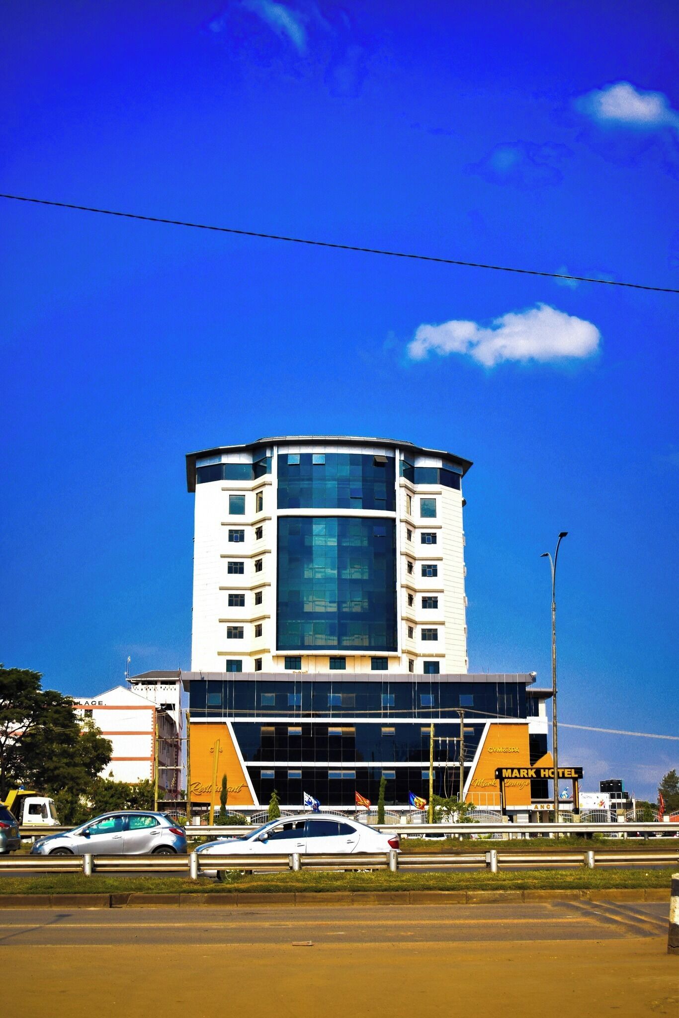 Un hotel moderno con una torre central de vidrio, un gimnasio y un spa, además de un estacionamiento con automóviles.