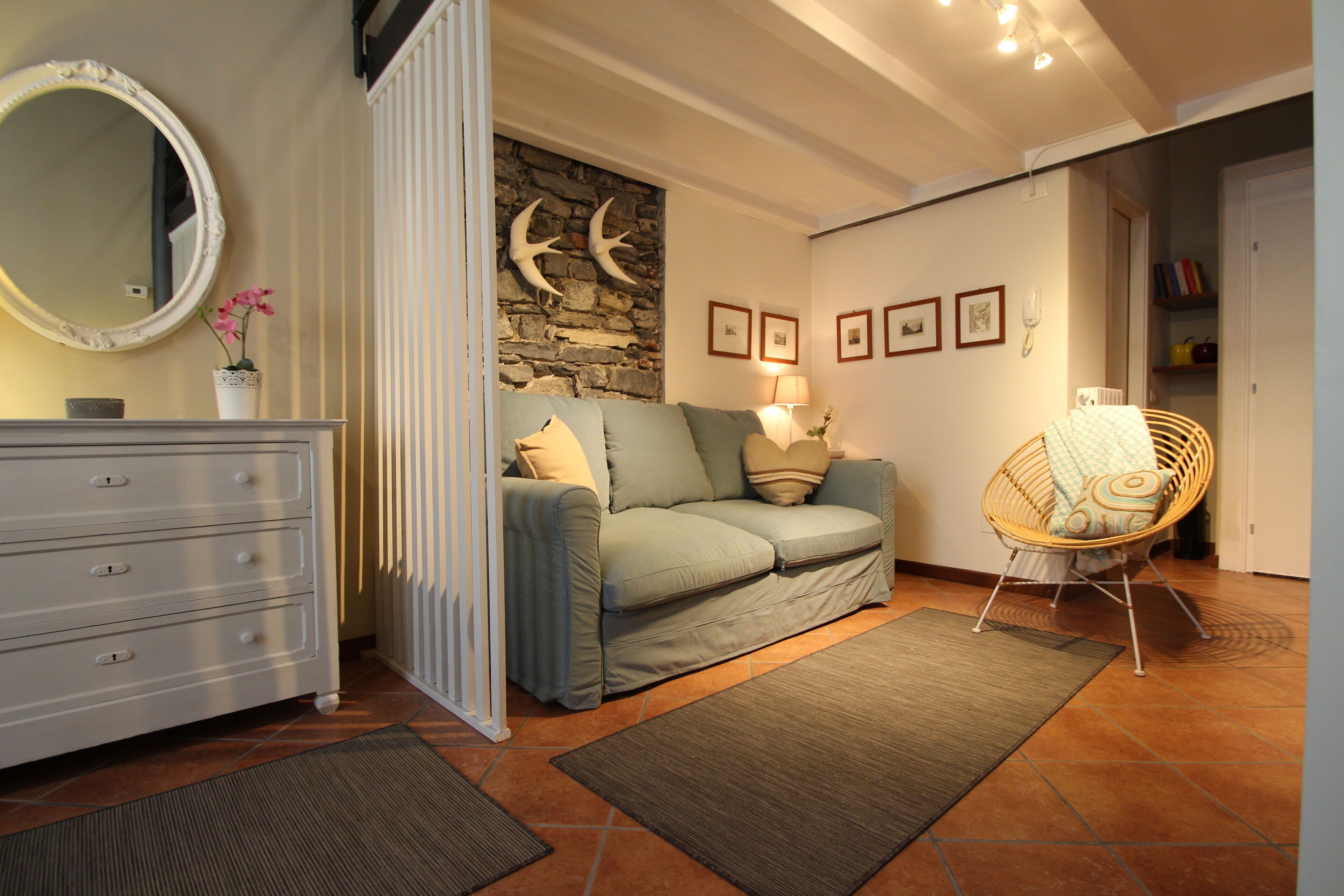 A cozy living room with a stone wall, a sofa, a chair, and a dresser.