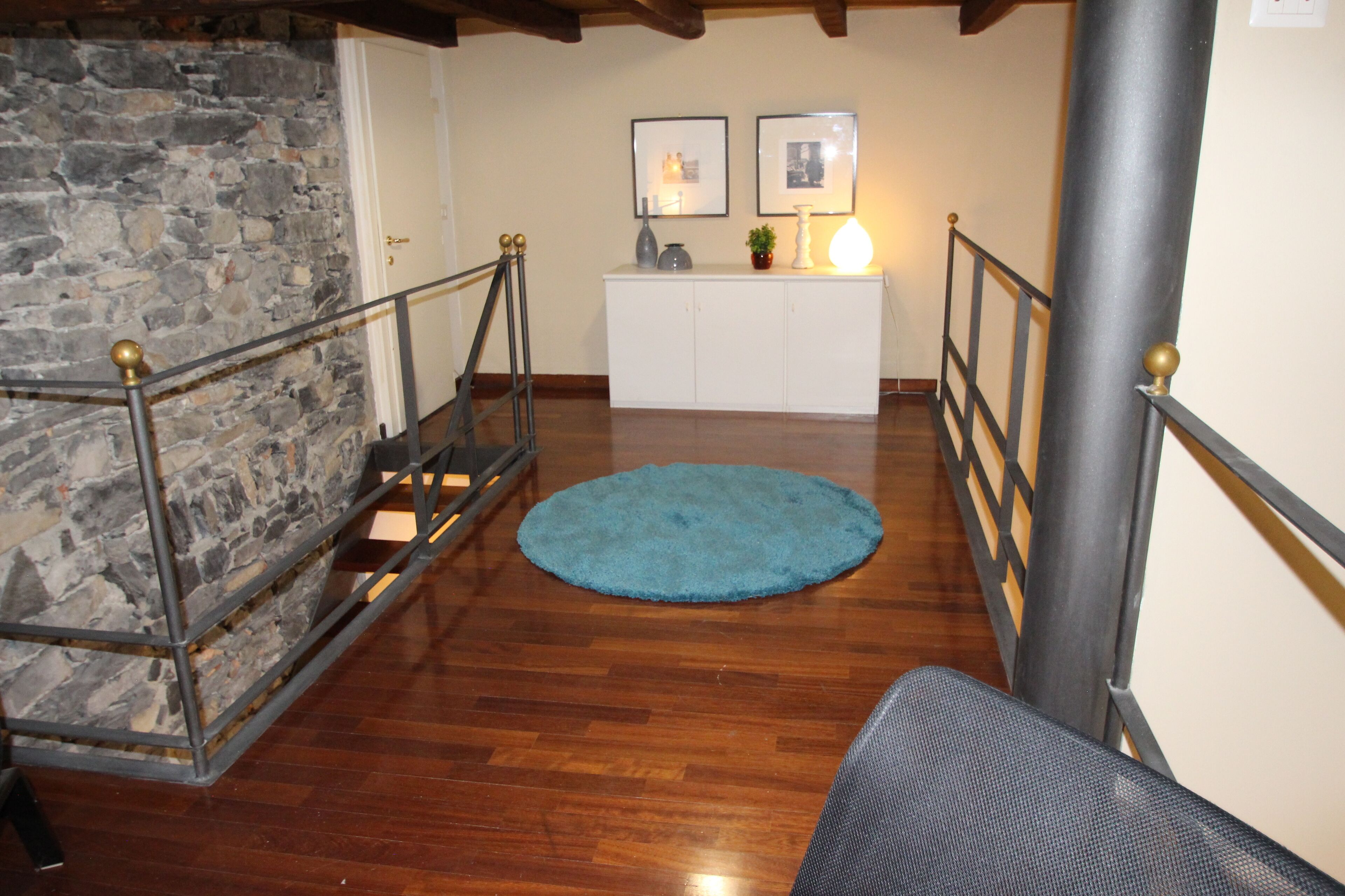 A staircase with a blue rug, wooden flooring, stone wall, white cabinet, and two framed pictures.