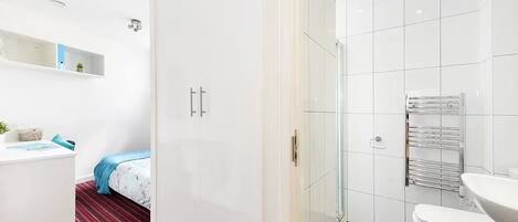 Una habitación de hotel moderna con una cama, un armario blanco, un baño con inodoro y ducha.
