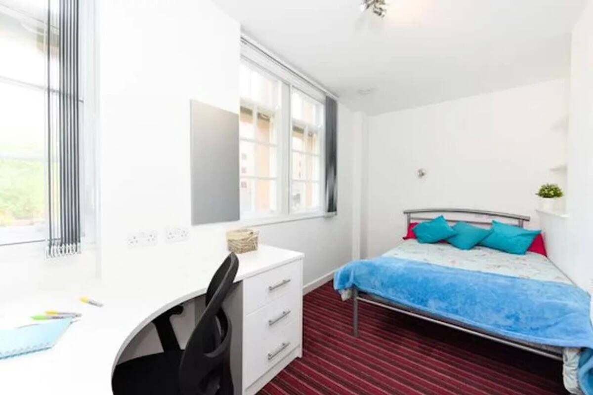 A bedroom with a bed, a desk, and a window.