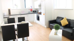 A modern kitchen with white cabinets, a black countertop, and a dining area with a white table and black chairs. - For Students Only Newarke St (Leicester)