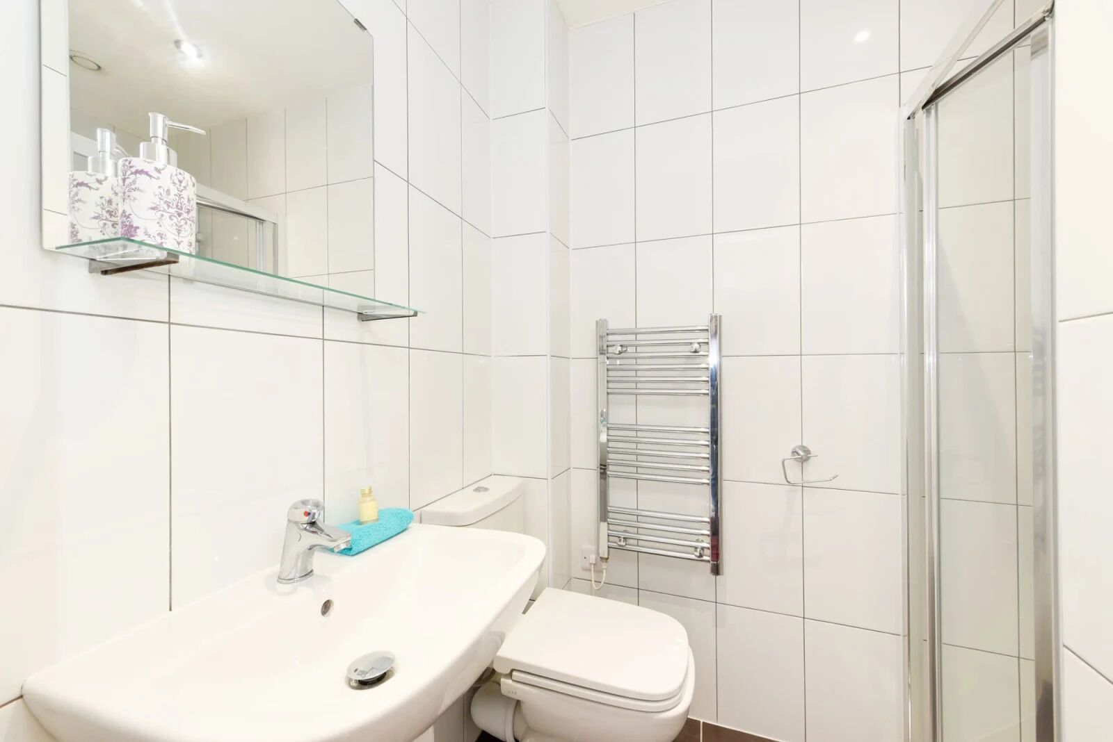 A bathroom with a white sink, a toilet, a glass shelf with toiletries, and a towel rack.