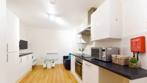 A modern kitchen with white cabinets, a black countertop, a microwave, and a fire blanket on the wall. - For Students Only Newarke St (Leicester)