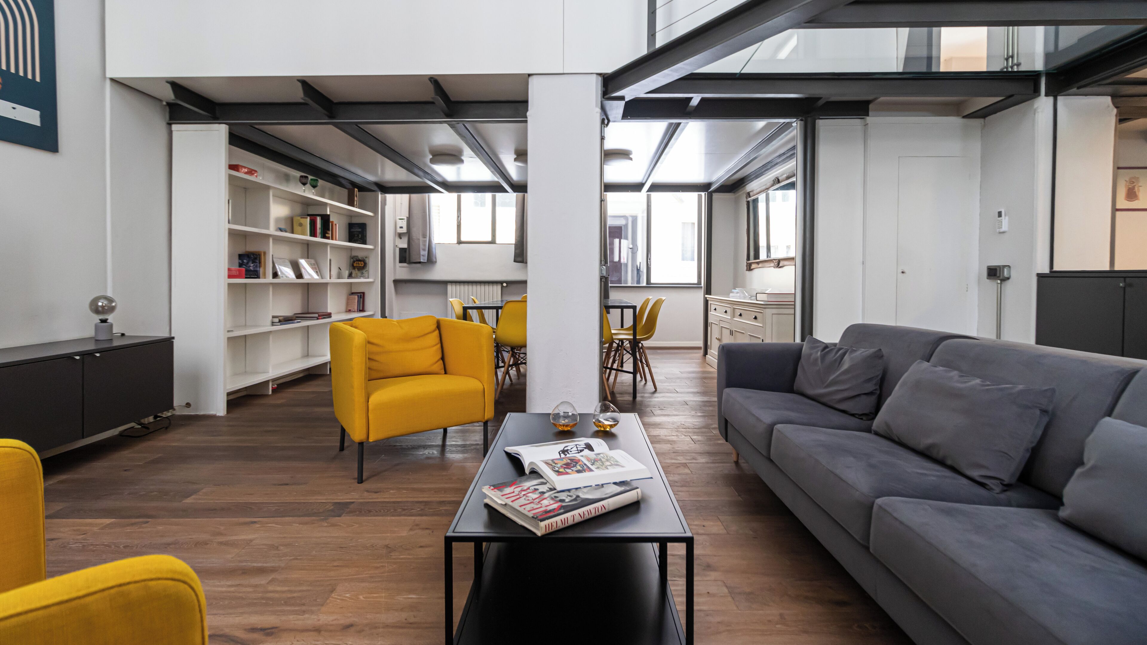 Un salon moderne avec un canapé gris, des fauteuils jaunes et une table basse sur laquelle sont posés des livres.