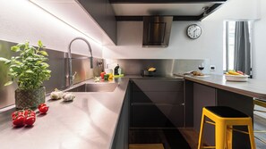 Uma cozinha moderna com pia de aço inoxidável, forno embutido e um relógio na parede.