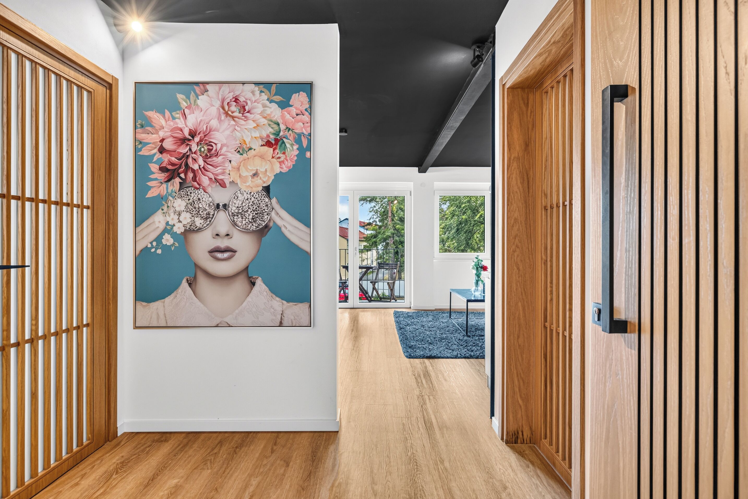 A hallway with wooden paneling, a large floral artwork on the wall, and a view of an outdoor area with a table and chairs.