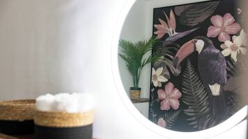 A round mirror reflecting a painting of a toucan and flowers, a potted plant, and a basket with white items on a shelf.