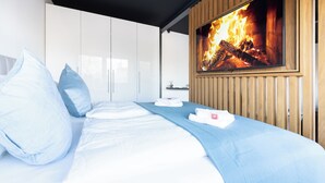 Une chambre d’hôtel moderne avec un lit, une armoire blanche et un écran de télévision diffusant une image de cheminée.