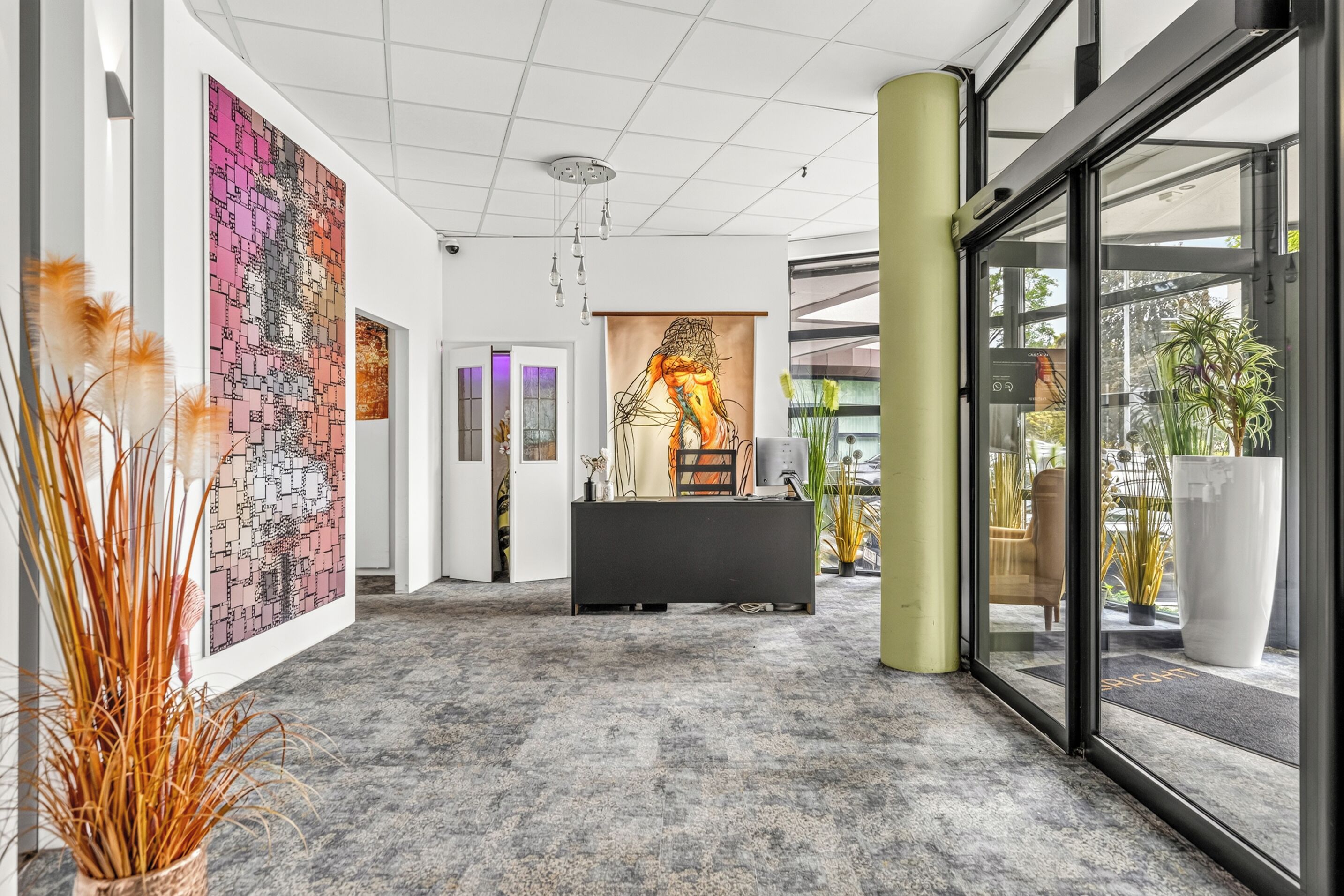 Eine moderne Lobby mit einer Rezeption, Kunstwerken an den Wänden und Blick ins Freie.