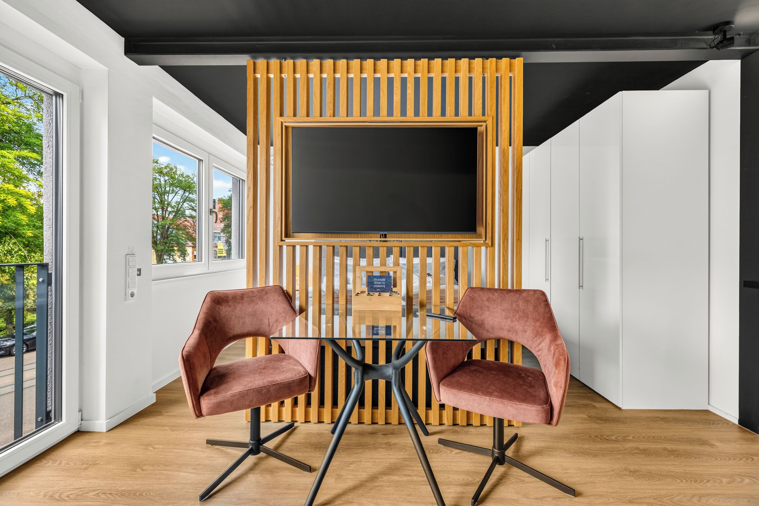 Un interno moderno con un tavolo in vetro, due sedie, una grande TV e una parete rivestita in legno.