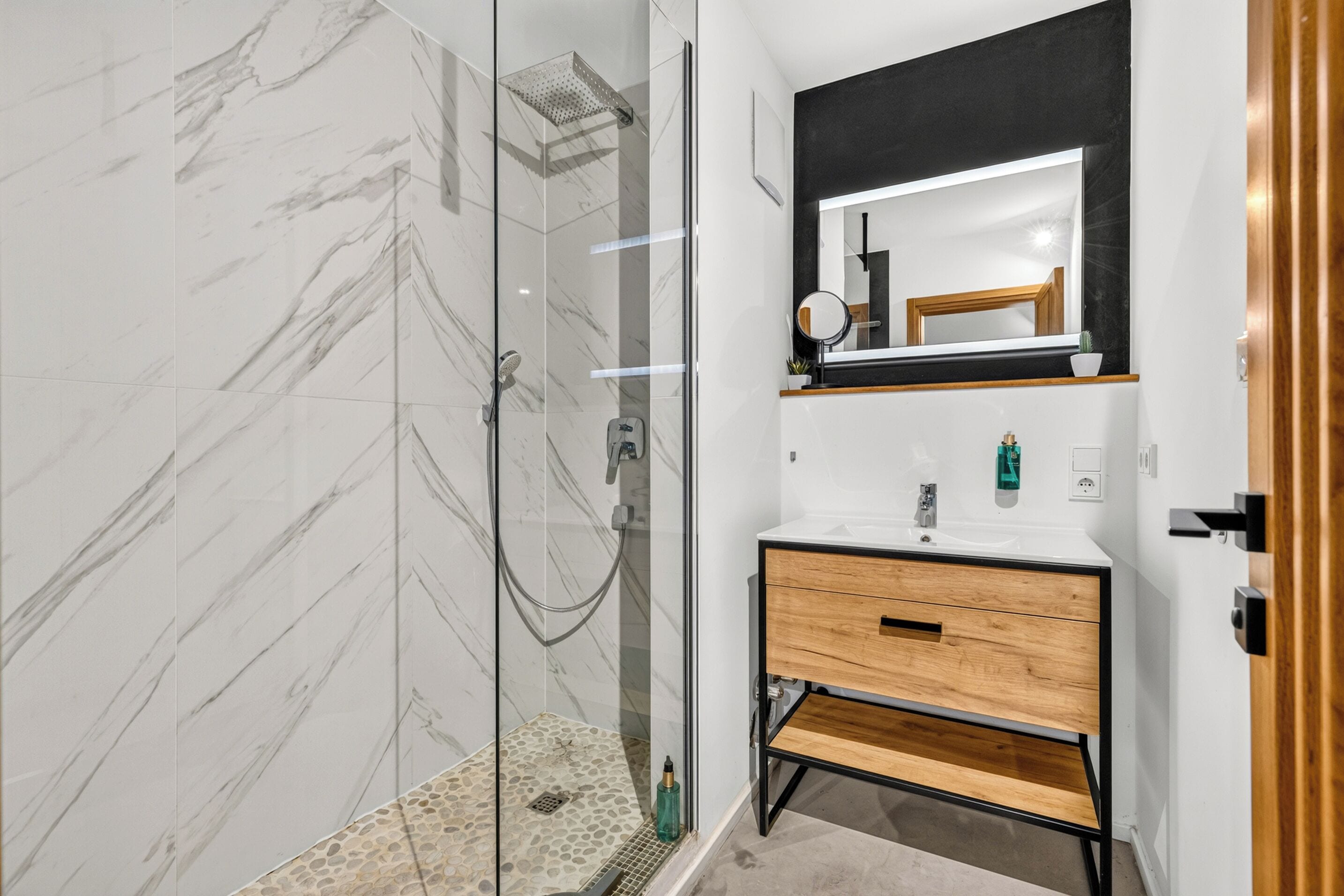A modern bathroom with a glass-enclosed shower, a wooden vanity, and a large mirror.