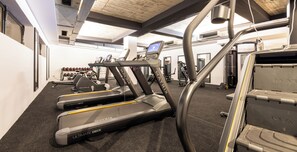Un gimnasio con cintas de correr, máquinas de pesas y un espejo grande.