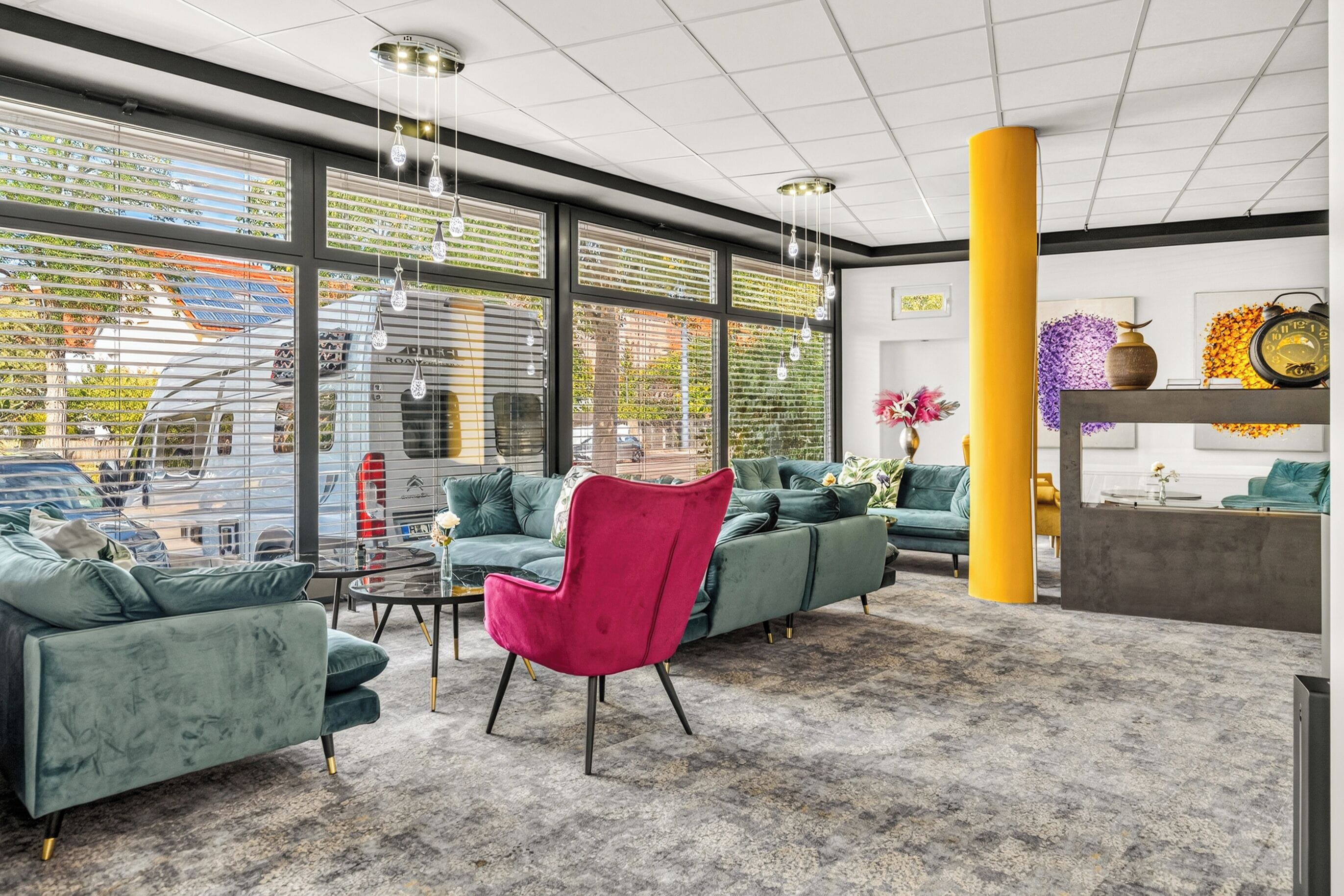 A modern interior with large windows, a green sofa set, a red chair, and a yellow pillar.
