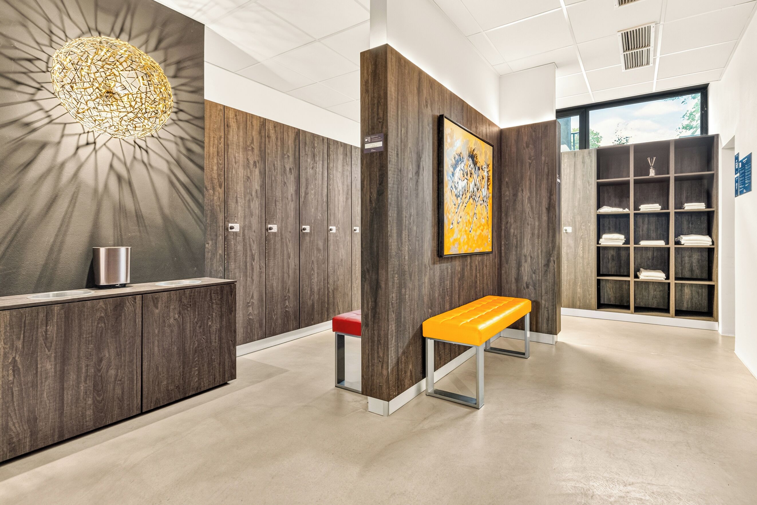 Uma área de recepção moderna com painel de parede de madeira, um banco, uma pia fixa na parede e uma grande pintura abstrata.