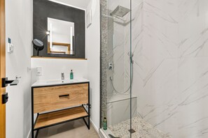 A modern bathroom with a wooden vanity, a glass shower enclosure, and a marble shower wall.