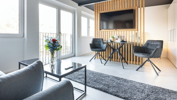 Un salon moderne avec une table basse en verre, deux canapés gris, un mur d’accent en bois et un téléviseur fixé au-dessus d’un panneau en bois.