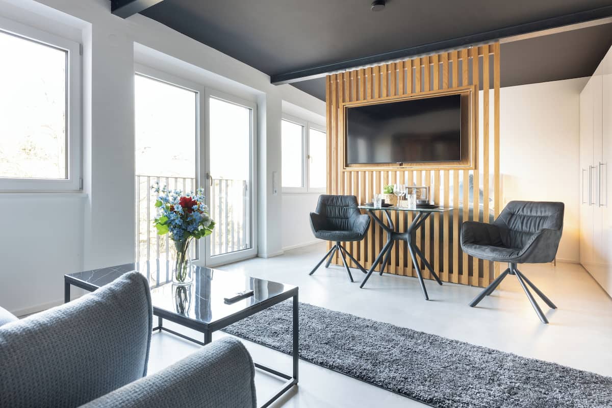 Ein modernes Wohnzimmer mit einem Glastisch, zwei grauen Sofas, einer Wandpaneele aus Holz und einem darüber montierten Fernseher.