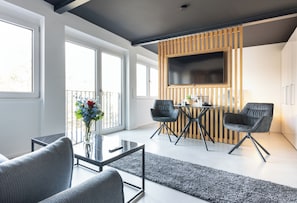 Un salon moderne avec une table basse en verre, deux canapés gris, un mur d’accent en bois et un téléviseur fixé au-dessus d’un panneau en bois.