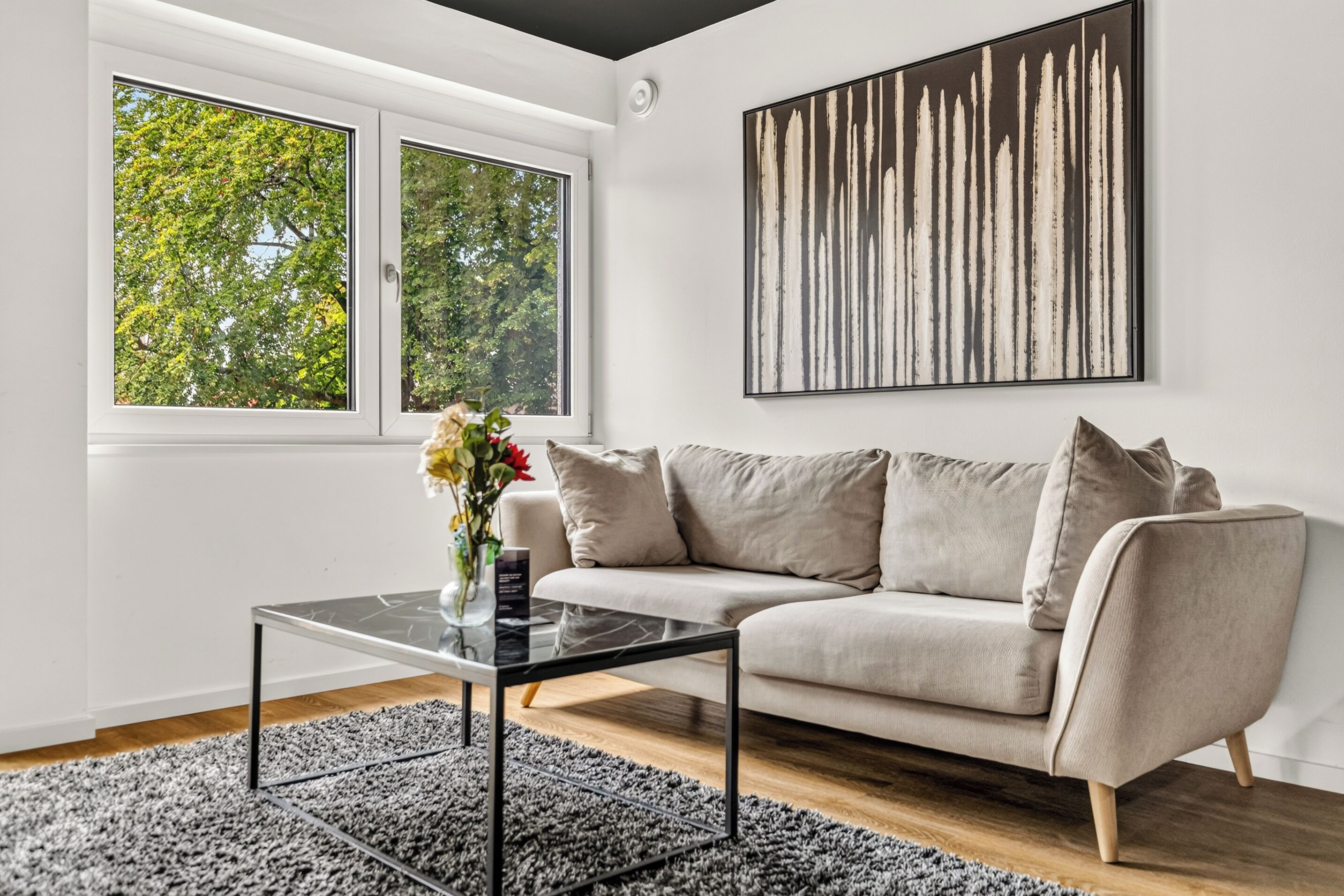 A modern living room with a sofa, a coffee table, and a large window with a view of trees.