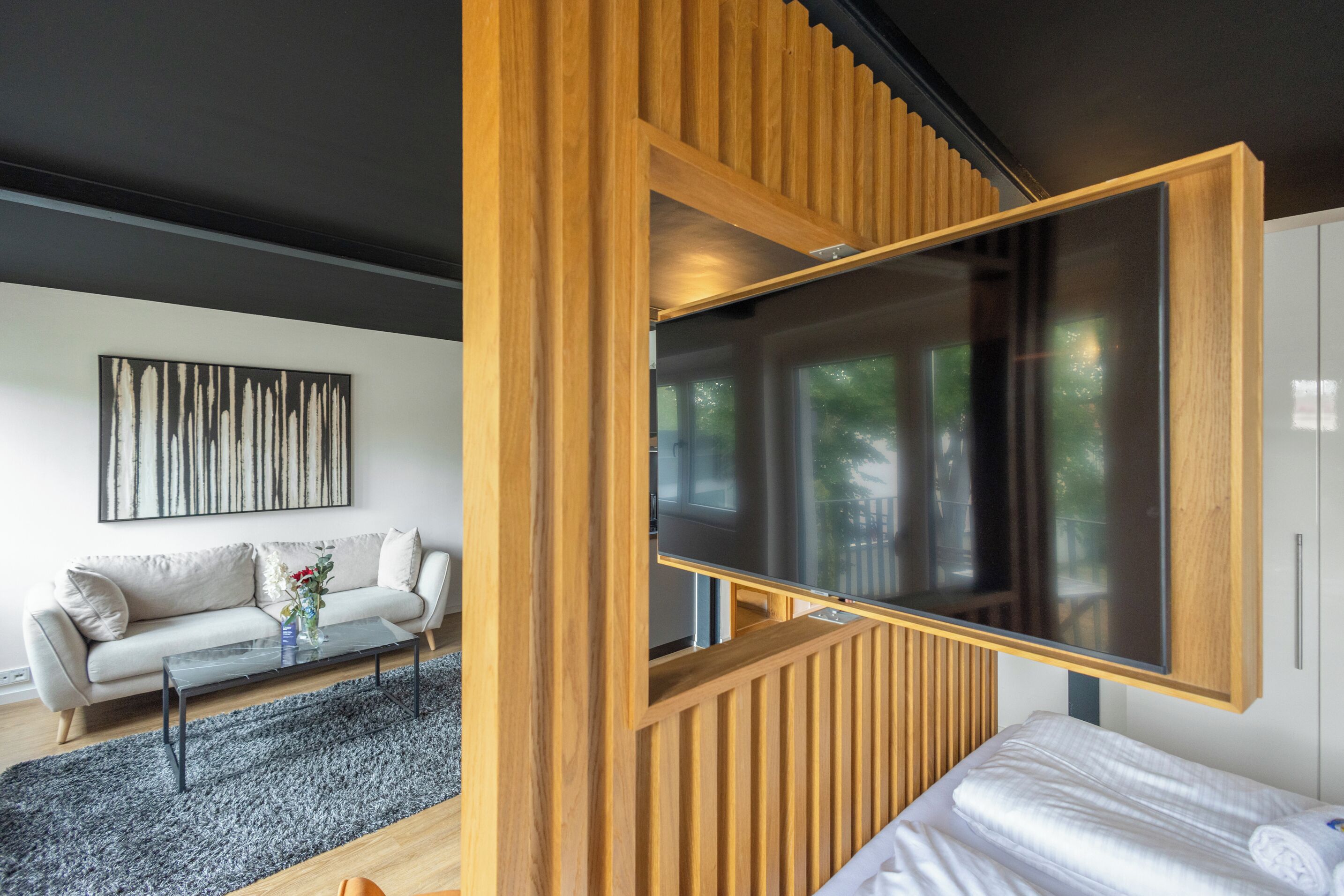 Un salon moderne avec un canapé, une table basse et une grande fenêtre ornée de lambris en bois.