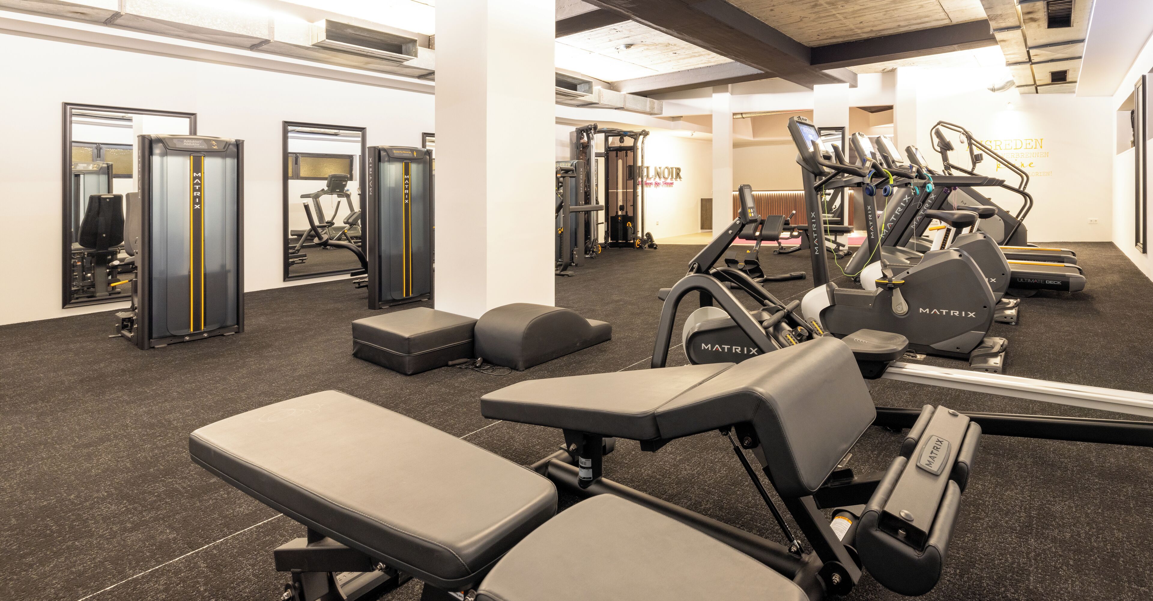 Ein Fitnessstudio mit unterschiedlichen Trainingsgeräten, darunter Laufbänder und Kraftgeräte.