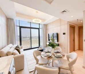 Uma sala de estar moderna com uma janela grande, uma área de jantar com mesa posta para quatro pessoas e um espaço de estar com um sofá.