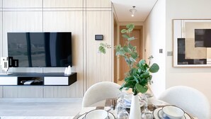 Un comedor moderno con pared de paneles de madera, un televisor de pantalla plana y una mesa de comedor dispuesta con platos, cubiertos y un jarrón con follaje verde.