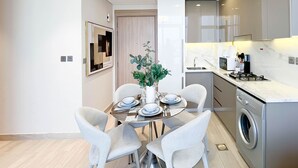 Una cocina moderna con lavadora integrada, un comedor con una mesa redonda y sillas blancas, y un espejo grande en la pared.