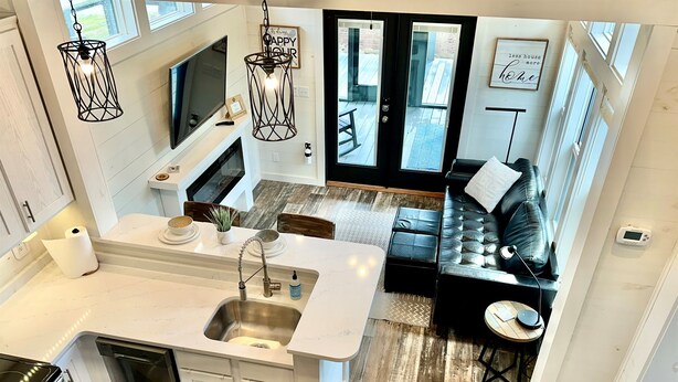 A modern kitchen with a central island, a dining area with a black leather sofa, and a living room with a black leather couch.