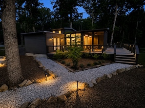 A modern house with a covered porch, a staircase, and a well-lit garden area.