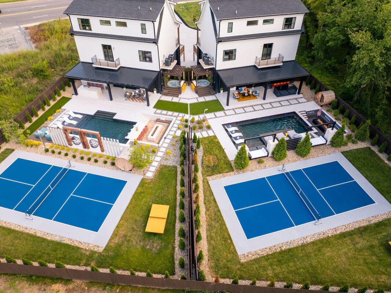 Una moderna casa a due piani con un cortile centrale, due campi da tennis, una piscina e zone relax all'aperto.