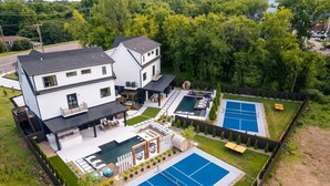 Ein modernes, zweistöckiges Haus mit großem Garten, inklusive Schwimmbad, Tennisplätzen und einer Terrassenfläche.