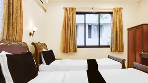 Quarto de hotel com duas camas, um guarda-roupa de madeira, uma escrivaninha e uma janela com cortinas.