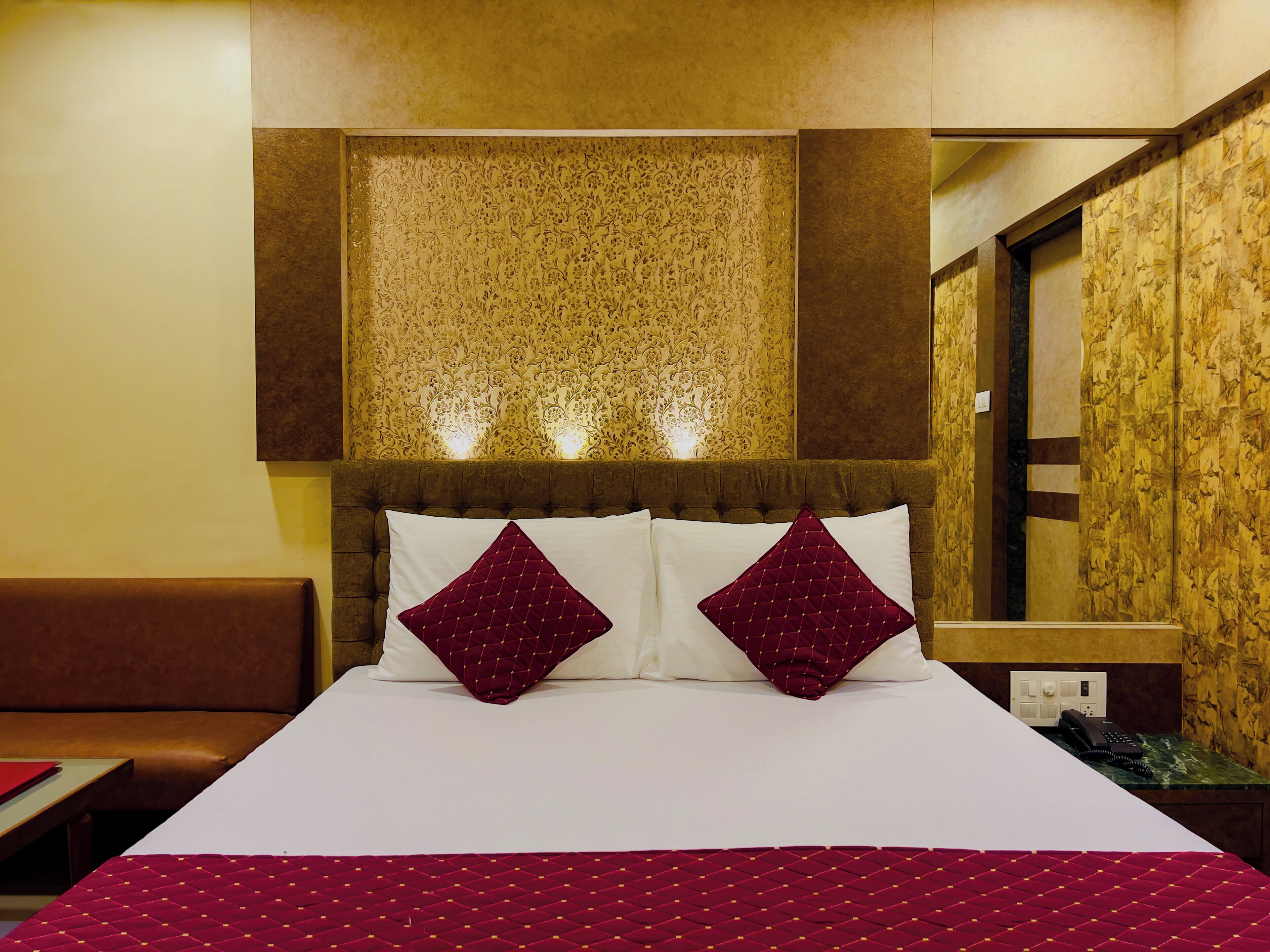Habitación de hotel con una cama grande, dos almohadones decorativos, cabecera con luces y pared de paneles de madera.