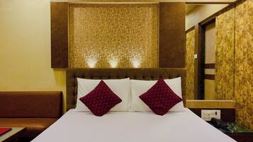Habitación de hotel con una cama grande, dos almohadones decorativos, cabecera con luces y pared de paneles de madera.