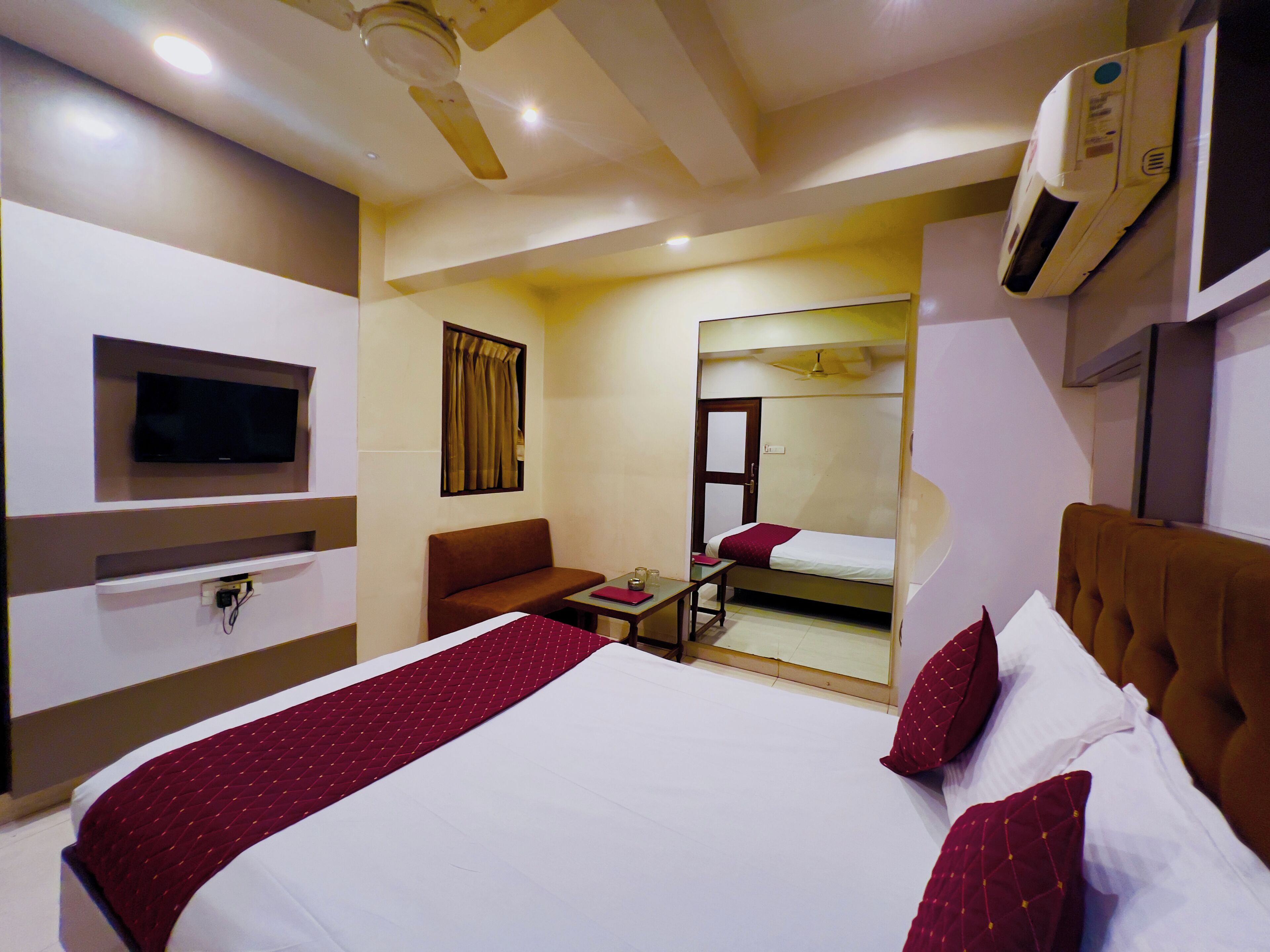 A hotel room with a bed, a TV mounted on the wall, a sofa, a small table, and a mirror.