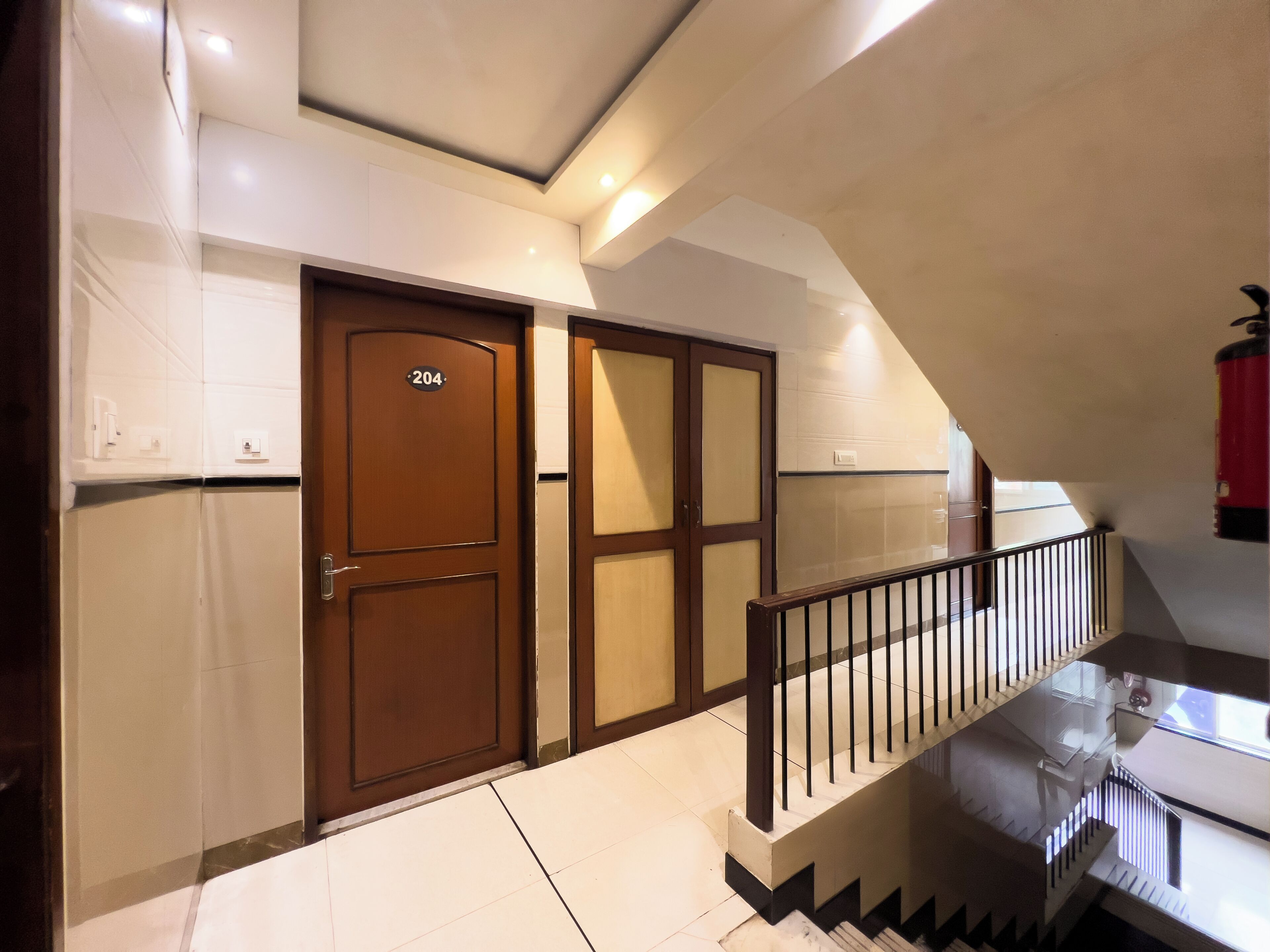 A modern interior with a wooden door marked '204', a staircase with a glass railing, and a tiled floor.