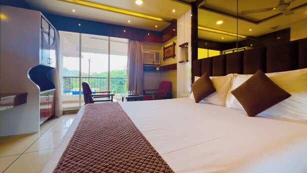 A hotel room with a large bed, a desk, a chair, and a balcony with a view. - Hotel Dwaraka (Mumbai)