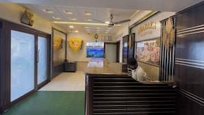 A reception area with a reception desk, a clock, and a wall with a framed picture. - Hotel Dwaraka (Mumbai)