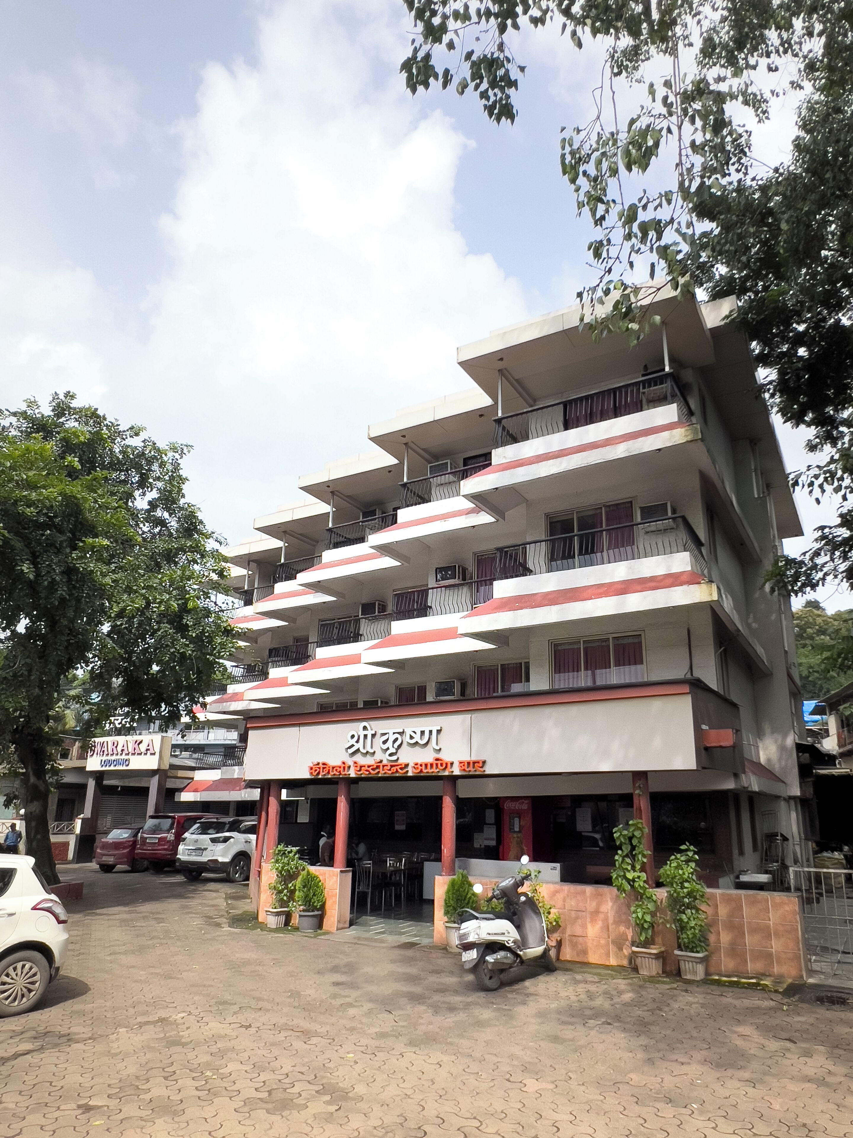 A multi-story building with a sign in a foreign language, potted plants, and parked vehicles.