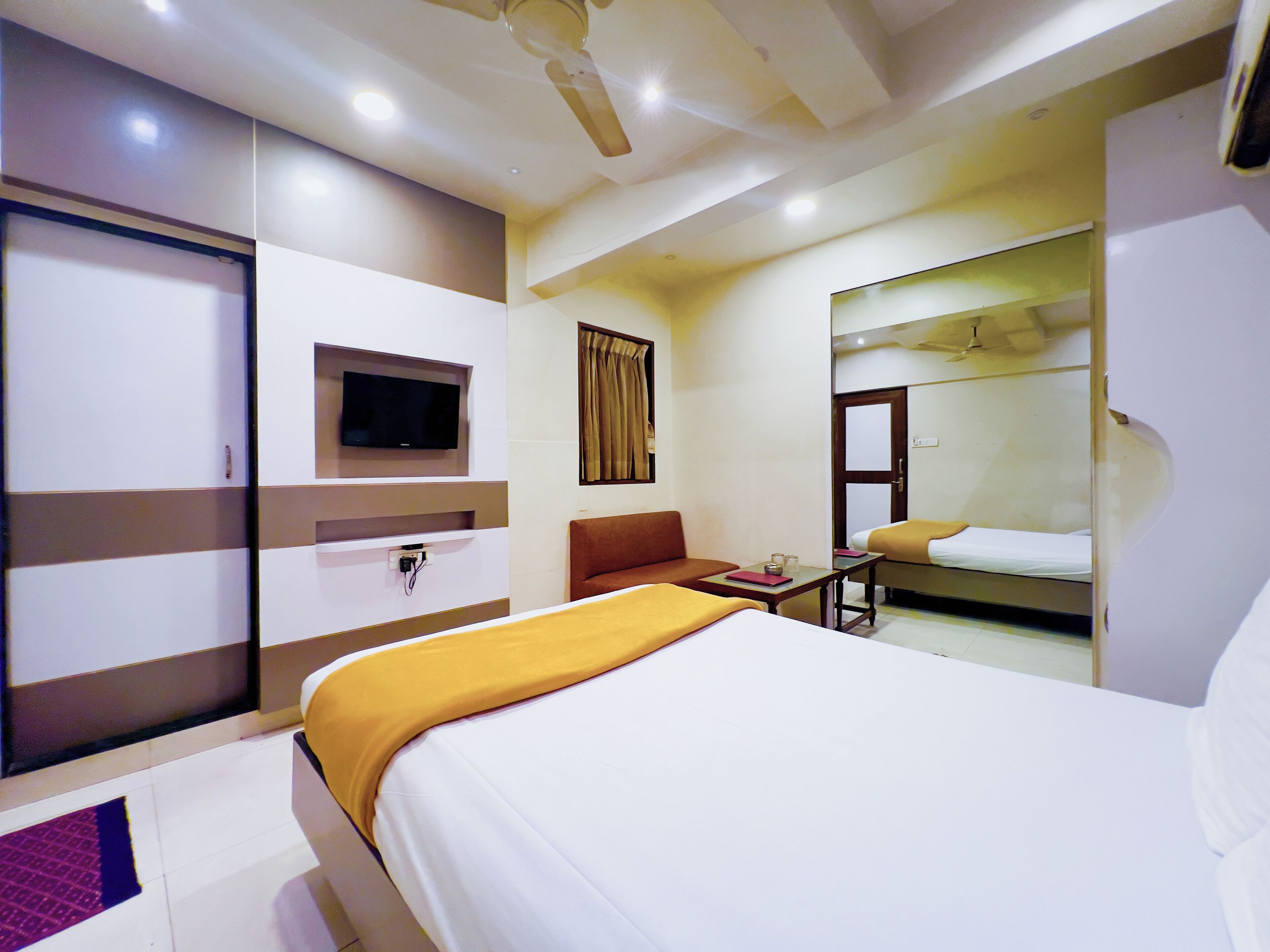 A hotel room with a bed, a TV mounted on the wall, a desk, and a wardrobe.